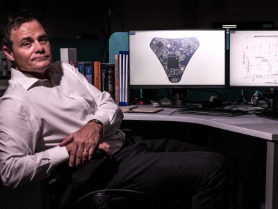 A man sits by a computer screen that shows wearable micro-technology