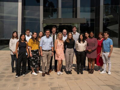 A team of researchers standing in the sun outside a building